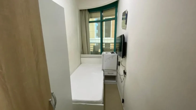 This picture shows a bed and screen inside a single room available for rent in Marina Dubai.